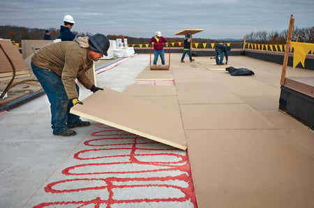 crew installing flat roof insulation with two-part adhesive