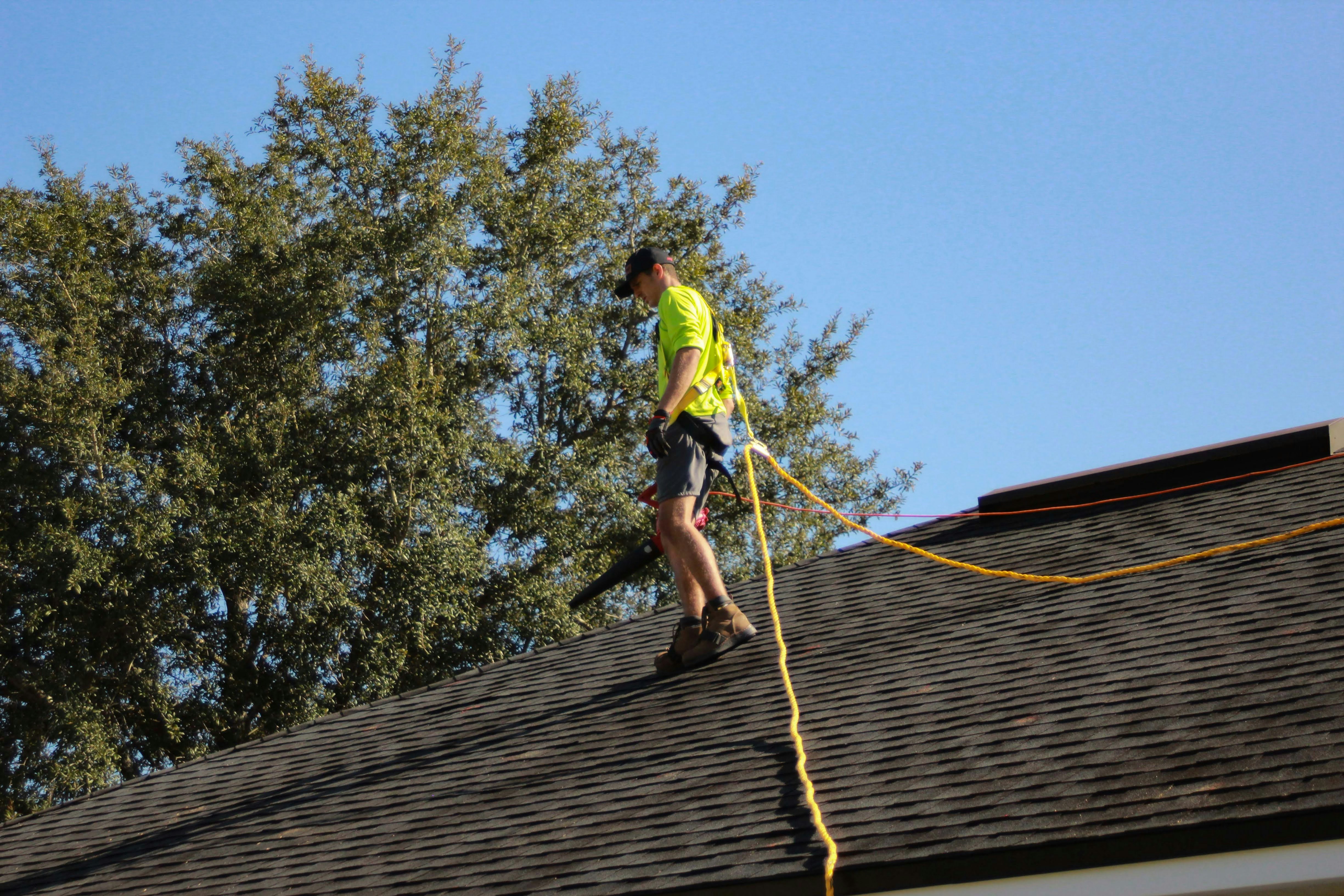 roofer walking a shingle roof with safety gear on